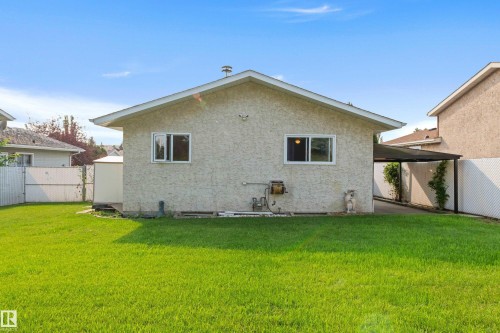 Expansive rear yard with a bright green lawn, stucco exterior, and a carport - 14538 37 Street Nw, Edmonton, AB 