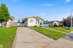 Single-story residence featuring light-colored siding, a concrete driveway, a front lawn, and a fenced side yard - 