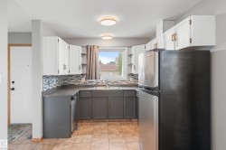 Kitchen featuring white upper cabinetry, dark gray lower cabinetry, mosaic tile backsplash, and a stainless steel refrigerator - 