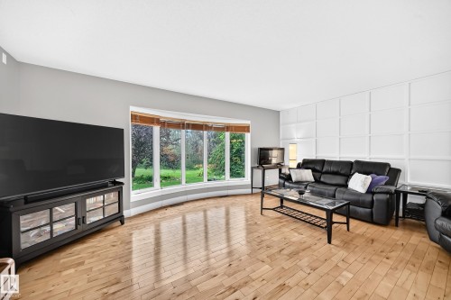 Expansive living area featuring light wood-finish flooring, a curved bay window, and a decorative grid wall panel accent - #38 24512 Sturgeon Rd, Rural Sturgeon County, AB 