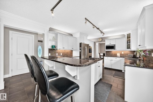 Kitchen featuring an island with dark stone countertops, white cabinetry with dark hardware, stainless steel appliances, and a tiled backsplash - #38 24512 Sturgeon Rd, Rural Sturgeon County, AB 