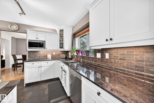 White cabinetry with black hardware, dark stone countertops, tile backsplash, built-in microwave, and stainless steel dishwasher - #38 24512 Sturgeon Rd, Rural Sturgeon County, AB 
