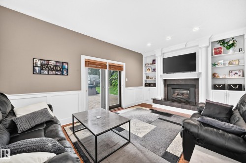 Fireplace with dark tile surround, built-in shelving, white wainscoting, sliding glass door, and wood-finish flooring - #38 24512 Sturgeon Rd, Rural Sturgeon County, AB 