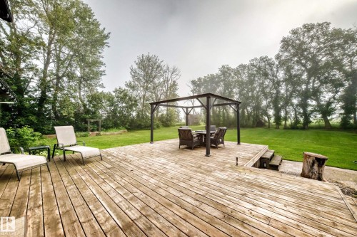Expansive wood-finish deck with a metal gazebo and integrated steps leading to a vast green lawn, bordered by mature trees - #38 24512 Sturgeon Rd, Rural Sturgeon County, AB 