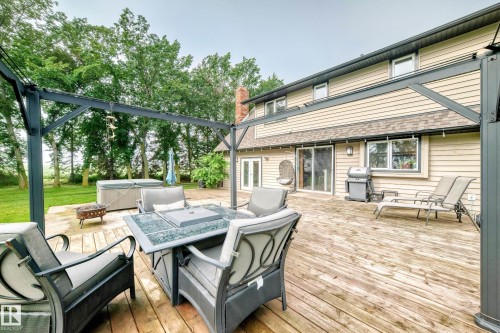 Expansive outdoor deck featuring a hot tub, a built-in fire pit, and a dark-toned pergola - #38 24512 Sturgeon Rd, Rural Sturgeon County, AB 