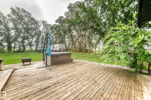 Expansive wood deck with a built-in spa, gravel hardscaping, and a lush green lawn surrounded by mature trees - #38 24512 Sturgeon Rd, Rural Sturgeon County, AB 