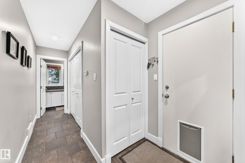 Hallway featuring dark tile flooring, white trim, and a utility room with a built-in vanity and window - #38 24512 Sturgeon Rd, Rural Sturgeon County, AB 