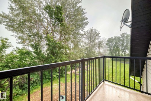 Balcony with black metal railings overlooking mature trees and a grassy area - #38 24512 Sturgeon Rd, Rural Sturgeon County, AB 