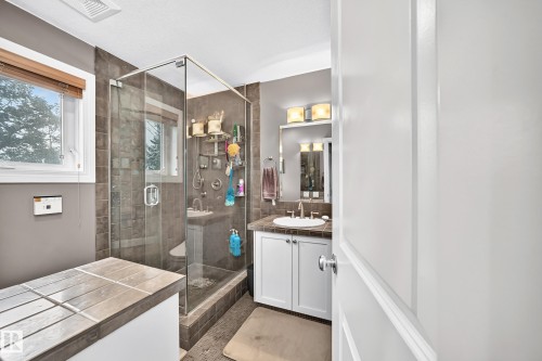 Glass-enclosed shower with dark tile surround, single vanity with undermount sink, and sconce lighting - #38 24512 Sturgeon Rd, Rural Sturgeon County, AB 