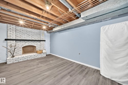 Exposed ceiling joists with visible utilities, painted brick fireplace with a dark mantel, wood-finish flooring, and light blue walls - #38 24512 Sturgeon Rd, Rural Sturgeon County, AB 