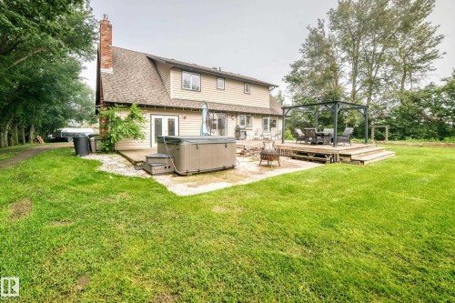 Expansive rear yard featuring a wooden deck with a built-in pergola, a hot tub, and a large lawn area - #38 24512 Sturgeon Rd, Rural Sturgeon County, AB 