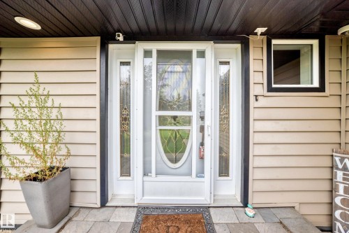 Entryway featuring a white door with decorative glass side panels, black trim, and horizontal siding - #38 24512 Sturgeon Rd, Rural Sturgeon County, AB 