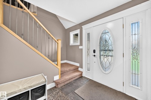 Entryway featuring a white door with decorative oval glass insert, two sidelight windows with patterned glass, and a staircase with light wood handrails and dark metal balusters - #38 24512 Sturgeon Rd, Rural Sturgeon County, AB 