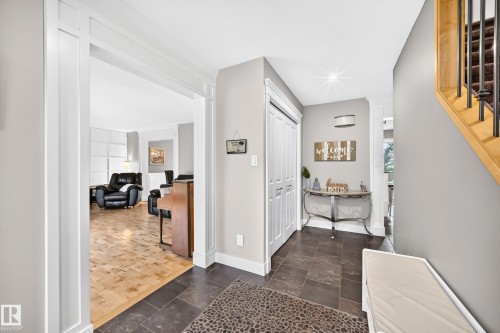 Hallway featuring dark tile flooring, a built-in closet with bi-fold doors, and a staircase with wood-finish treads and metal balusters - #38 24512 Sturgeon Rd, Rural Sturgeon County, AB 
