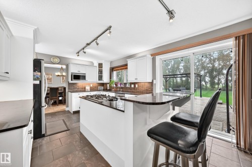 Kitchen featuring white cabinetry, dark countertops, a built-in microwave, and a gas stovetop on the island - #38 24512 Sturgeon Rd, Rural Sturgeon County, AB 