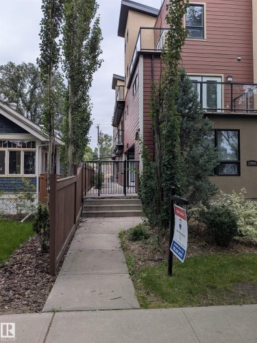 Concrete walkway leading to exterior stairs, featuring a wood fence, mature trees, and shrubs - 10806 83 Avenue Nw, Edmonton, AB - Outdoor With Balcony