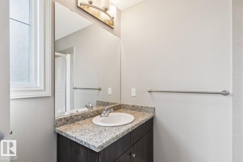 Dark wood-finish vanity with an undermount sink, speckled countertop, and chrome faucet - 5409 3 Avenue Sw, Edmonton, AB - Indoor Photo Showing Bathroom