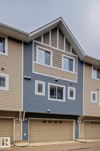 Multi-level exterior with a prominent gable roofline, featuring horizontal siding in two tones, multiple windows with white trim, and an integrated garage with a panel door - 5409 3 Avenue Sw, Edmonton, AB - Outdoor