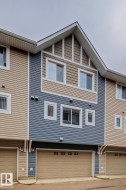 Multi-level exterior with a prominent gable roofline, featuring horizontal siding in two tones, multiple windows with white trim, and an integrated garage with a panel door - 