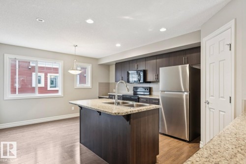 Kitchen island with integrated double basin sink, granite countertop, stainless steel appliances, dark wood-finish cabinetry, and wood-finish flooring - 5409 3 Avenue Sw, Edmonton, AB - Indoor Photo Showing Kitchen With Double Sink