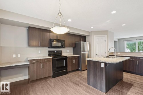 Kitchen featuring wood-finish flooring, dark wood cabinetry, light-toned countertops, a central island with an undermount sink, and recessed lighting - 5409 3 Avenue Sw, Edmonton, AB - Indoor Photo Showing Kitchen With Double Sink