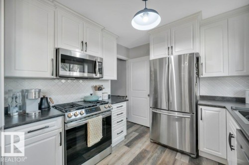 White shaker cabinetry, stainless steel appliances, dark countertops, patterned tile backsplash, and vinyl plank flooring - #138 5231 51 St, Bon Accord, AB - Indoor Photo Showing Kitchen With Upgraded Kitchen