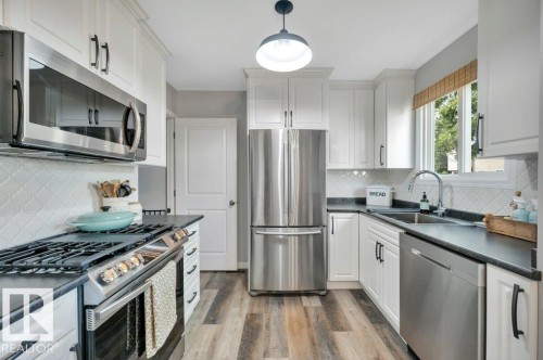White cabinetry with matte black hardware, stainless steel appliances, dark countertops, vinyl plank flooring, and white patterned tile backsplash - #138 5231 51 St, Bon Accord, AB - Indoor Photo Showing Kitchen With Upgraded Kitchen