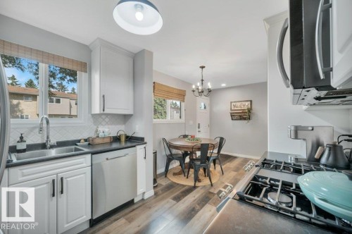 White cabinetry with dark hardware, stainless steel appliances, dark countertops, vinyl plank flooring, and a white subway tile backsplash - #138 5231 51 St, Bon Accord, AB - Indoor Photo Showing Kitchen
