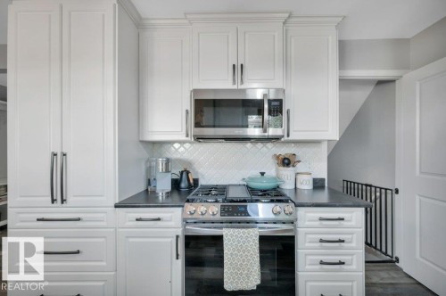 White cabinetry with dark pulls, stainless steel appliances, dark countertop, and decorative tile backsplash - #138 5231 51 St, Bon Accord, AB - Indoor Photo Showing Kitchen