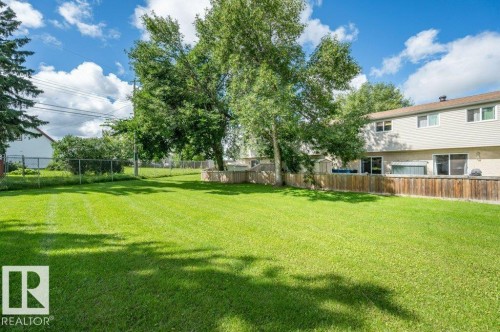 Expansive green lawn, mature trees, wood fence, chain-link fence, and a two-story exterior with multiple windows - #138 5231 51 St, Bon Accord, AB - Outdoor