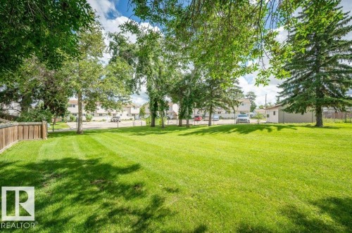Expansive grass lawn with mature trees and a wood-panel fence - #138 5231 51 St, Bon Accord, AB - Outdoor