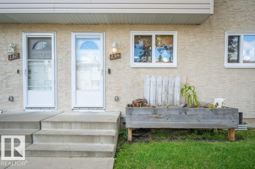 Stucco exterior with white trim, two entry doors with storm doors, and two windows - #138 5231 51 St, Bon Accord, AB - Outdoor With Deck Patio Veranda