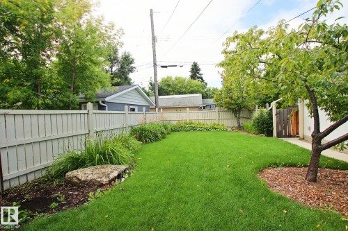 Expansive lawn featuring a privacy fence, mature trees, landscaped garden beds, and a wood gate - 5712 113B Street Nw, Edmonton, AB - Outdoor
