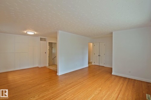 Hardwood flooring, flush-mount ceiling light fixture, panel accent wall, and bi-fold doors - 5712 113B Street Nw, Edmonton, AB - Indoor Photo Showing Other Room