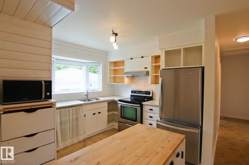 Kitchen featuring a bay window, wood-finish flooring, white cabinetry, integrated stainless steel appliances, and a wood butcher block island - 5712 113B Street Nw, Edmonton, AB - Indoor Photo Showing Kitchen With Double Sink
