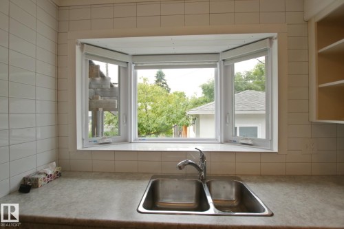 Dual basin stainless steel sink with chrome faucet, bay window, light-colored countertop, and white tiled walls - 5712 113B Street Nw, Edmonton, AB - Indoor Photo Showing Kitchen With Double Sink