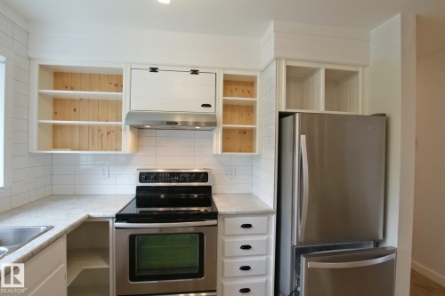 Modern kitchen featuring stainless steel appliances, white subway tile backsplash, white shaker-style cabinetry with matte black hardware, and light-toned countertops - 5712 113B Street Nw, Edmonton, AB - Indoor Photo Showing Kitchen