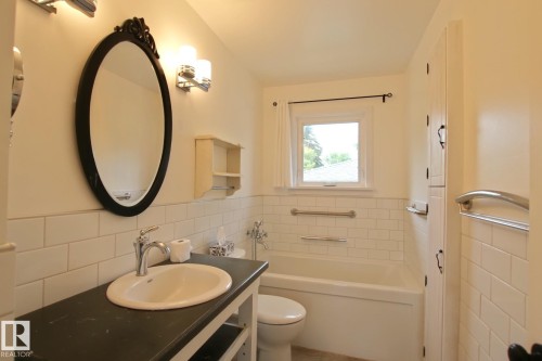 White subway tile wainscoting, built-in tub with grab bars, and a vanity with an oval basin sink - 5712 113B Street Nw, Edmonton, AB - Indoor Photo Showing Bathroom