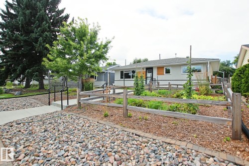 Front exterior featuring a wood fence, mature landscaping, stone ground cover, concrete walkways, and an asphalt shingle roof - 5712 113B Street Nw, Edmonton, AB - Outdoor