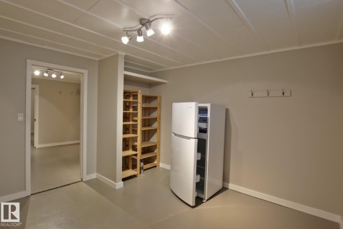 Track lighting illuminates a room with light gray walls and a light gray floor, featuring built-in wooden shelving - 5712 113B Street Nw, Edmonton, AB - Indoor Photo Showing Other Room