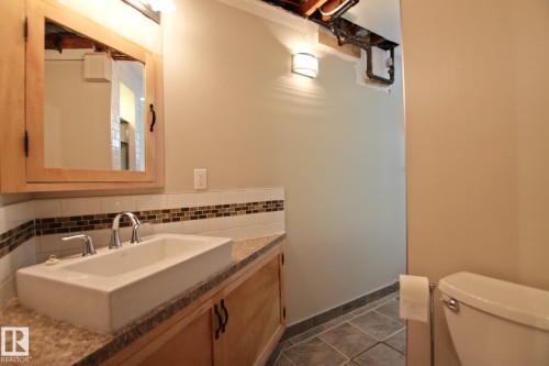 Vessel sink with chrome faucet, wood-finish vanity with countertop, tiled backsplash, and tiled flooring - 5712 113B Street Nw, Edmonton, AB - Indoor Photo Showing Bathroom
