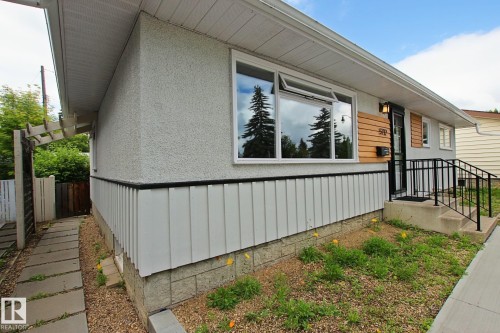 Stucco exterior with wood accent paneling, white window frames, concrete steps, and a black metal handrail - 5712 113B Street Nw, Edmonton, AB - Outdoor With Deck Patio Veranda With Exterior