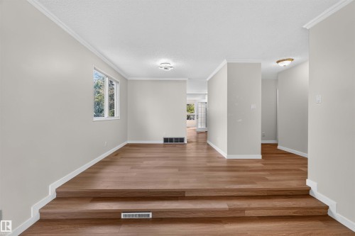 Wood-finish flooring with a multi-level design, crown molding, white trim, and a window with outdoor scenery - 14725 43A Avenue Nw, Edmonton, AB - Indoor Photo Showing Other Room