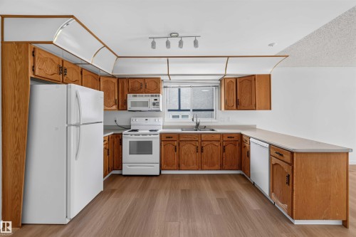 Kitchen featuring wood-finish cabinetry, white appliances, track lighting, and wood-finish flooring - 14725 43A Avenue Nw, Edmonton, AB - Indoor Photo Showing Kitchen With Double Sink