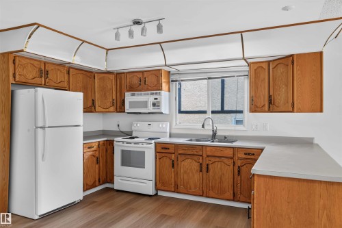 Kitchen featuring wood-finish cabinetry, white appliances, a window above the sink, track lighting, and wood-finish flooring - 14725 43A Avenue Nw, Edmonton, AB - Indoor Photo Showing Kitchen With Double Sink