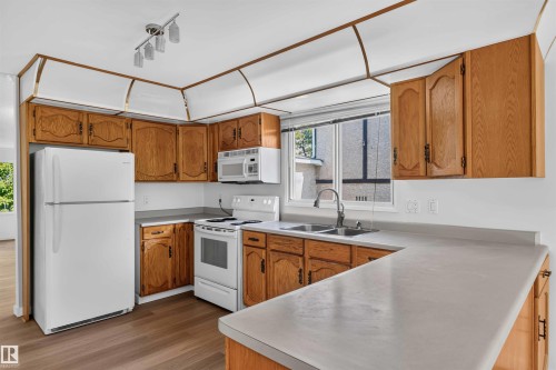 Kitchen featuring wood-finish cabinetry, white appliances, track lighting, and a double-basin sink - 14725 43A Avenue Nw, Edmonton, AB - Indoor Photo Showing Kitchen With Double Sink