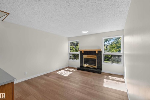 Wood-finish flooring, recessed lighting, and a dark stone fireplace with a natural wood mantel - 14725 43A Avenue Nw, Edmonton, AB - Indoor Photo Showing Other Room With Fireplace