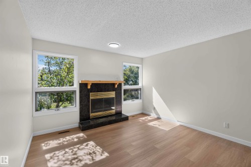 Wood-finish flooring throughout, featuring a fireplace with a black surround and a wood mantel - 14725 43A Avenue Nw, Edmonton, AB - Indoor Photo Showing Living Room With Fireplace
