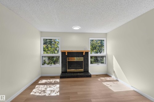 Fireplace with a black tile surround and hearth, wood mantel, and brass-tone insert - 14725 43A Avenue Nw, Edmonton, AB - Indoor Photo Showing Other Room With Fireplace