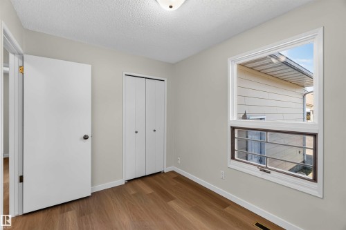 Neutral wall paint, wood-finish flooring, white bi-fold closet doors, and a window with white trim - 14725 43A Avenue Nw, Edmonton, AB - Indoor Photo Showing Other Room